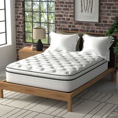 a bed with white sheets and pillows in a room next to a brick wall,