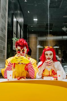 two clowns dressed in yellow and red are sitting at a table with their mouths open