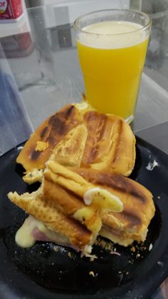 a black plate topped with waffles next to a glass of orange juice