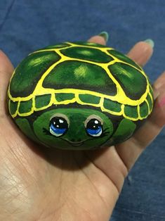 a hand holding a painted rock with a turtle on it's face and eyes