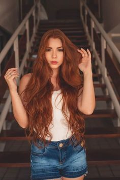 a woman with long red hair standing in front of stairs and looking at the camera