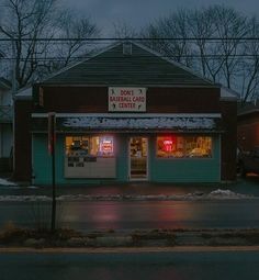 an empty street in front of a store at night with snow on the ground and cars parked outside