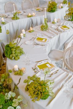 the table is set with white linens and green flowers, candles and place settings