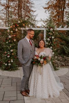 a bride and groom pose for a photo in front of an arch decorated with flowers