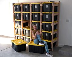 a woman sitting on top of two bins in front of a book shelf filled with black and yellow boxes