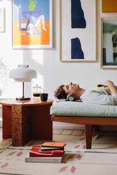 a man laying on top of a bed next to a table with a lamp and books