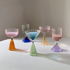 five different colored glass vases sitting on a white table top, with one in the middle