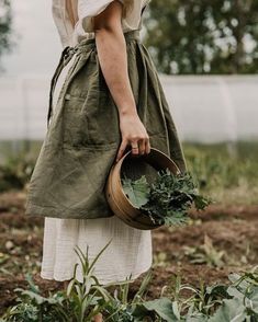 a woman holding a bucket full of greens in her hands while walking through a field