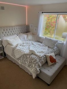 a white bed sitting next to a window in a bedroom under a light that is on