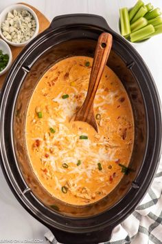 a crock pot filled with chicken and cheese soup next to some celery