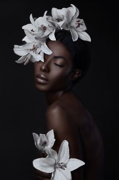 a woman with white flowers on her head and black skin, in front of a dark background