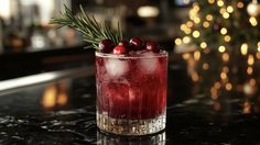 a drink with cranberries and rosemary garnish in a glass on a bar