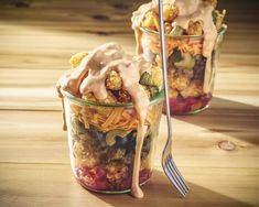 two glass jars filled with food on top of a wooden table next to a fork