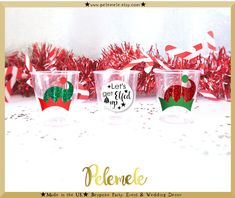 three plastic cups with red and green designs on them sitting in front of tinsel