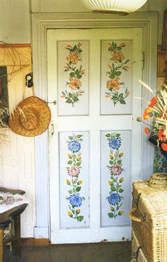 a white door with flowers painted on the side and wicker baskets hanging from it