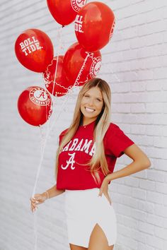 a woman standing in front of a brick wall with red balloons