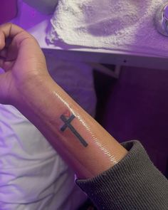 a person with a small cross tattoo on their left arm and wrist, in front of a purple light