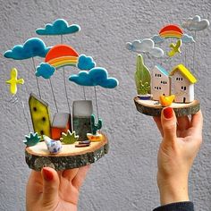 two hands holding small houses and clouds in the air, one is made out of wood