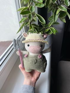 a hand holding a small stuffed animal next to a potted plant on a window sill