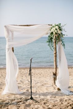 an outdoor ceremony setup on the beach with white draping and greenery draped over it