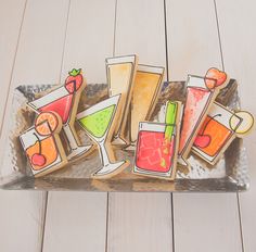 cookies decorated with different types of cocktails on a metal platter sitting on a wooden table