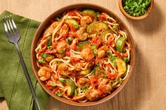 a bowl of pasta with shrimp, zucchini and peppers next to a fork