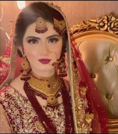 a woman in a red and gold bridal outfit with jewelry on her head, posing for the camera