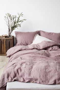 an unmade bed with pink linens in a white room next to a plant