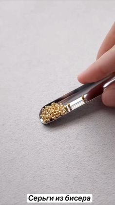 a person holding a small metal object with gold beads on it's tip and finger