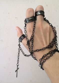 a hand with chains and rings on it, holding a cross in the middle of it