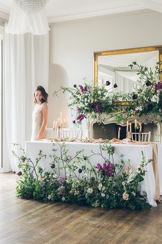 a woman standing in front of a table with flowers and candles on top of it