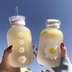 two people holding up mason jars with daisies on the front and sides, one has a straw in it