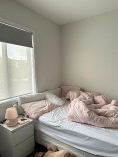 an unmade bed with pink sheets and pillows in a bedroom next to a window