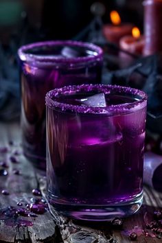 two glasses filled with purple liquid next to candles