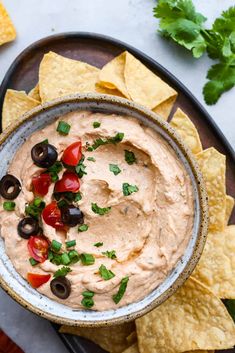 a bowl filled with black olives and tomatoes surrounded by tortilla chips on a plate