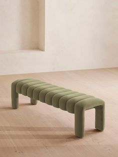 a green bench sitting on top of a hard wood floor next to a white wall