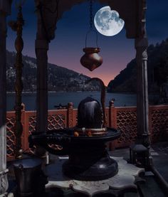 a full moon is seen over the water from an outdoor gazebo in front of a mountain range