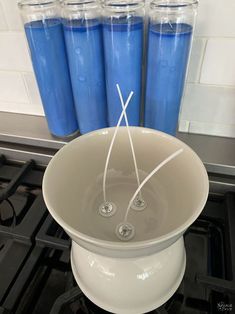 three blue candles sitting on top of a stove next to a bowl with water in it