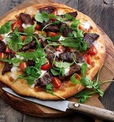 a pizza topped with meat and veggies on top of a wooden cutting board