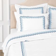 a white bed with blue scalloped trim on the headboard and pillow cases