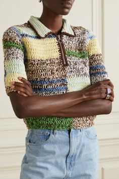 a woman with her arms crossed wearing a multicolored knitted sweater and jeans