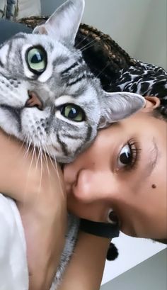 a woman holding a cat in her arms while laying on top of a bed next to a wall