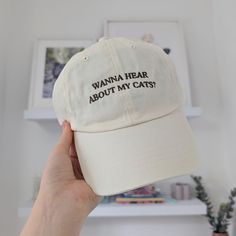 a person holding up a white hat with the words wanna hear about my cat?