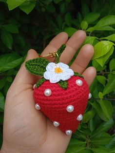 a hand holding a crocheted strawberry with a white flower on it's side