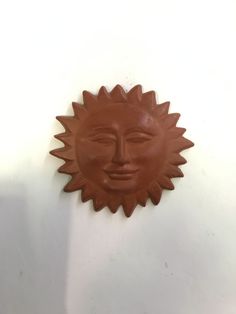 a clay sun face hanging on the wall in front of a white wall with no one around it