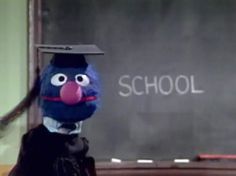 the sesame street character is standing in front of a chalkboard and wearing a mortar cap