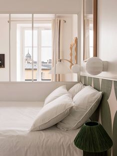 a bed with white sheets and pillows next to a large window in a small room