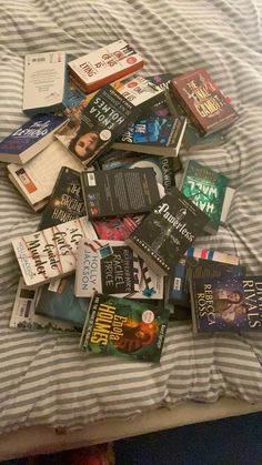 a pile of books sitting on top of a bed next to a striped comforter