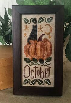 a cross stitch picture frame with a pumpkin on it and the words october written in black