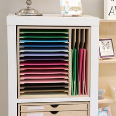 a white bookcase with many different colored papers in it and a lamp on top